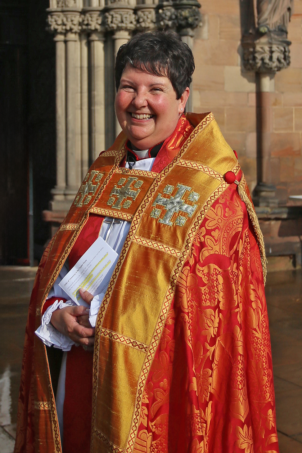 Bishop Jan in her red and gold cathedral robes stood in bright sunshine outside the west door of the cathedral 