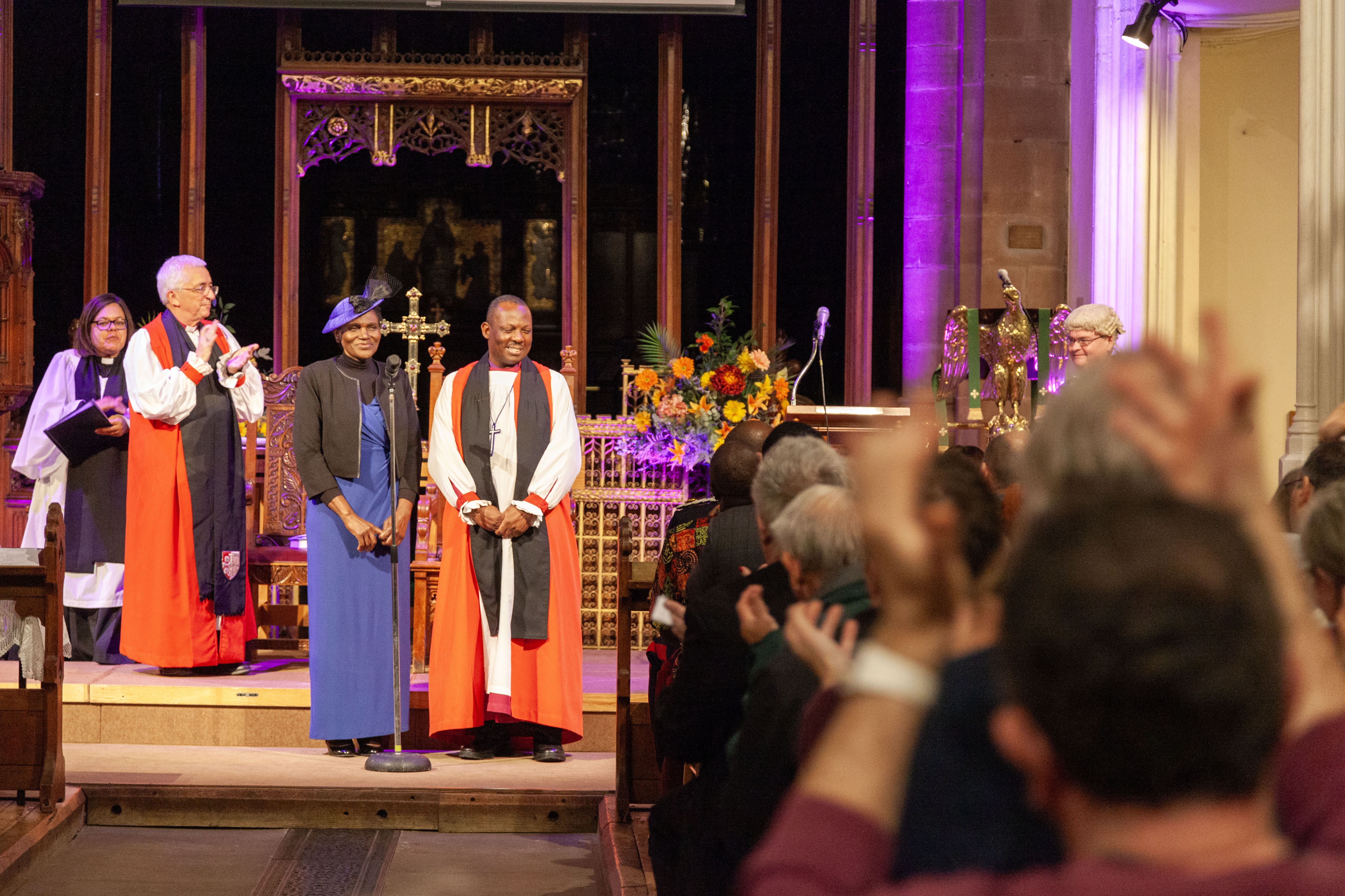 Bishop Tim Wambunya and his wife Gertrude greeted with applause at his Welcome service in St Matthew's church, Walsall 15 Oct 2024. The image shows, (left to right) Bishop Michael clapping, Gertrude, Bishop Tim, and on the right and in the foreground, congregation clapping